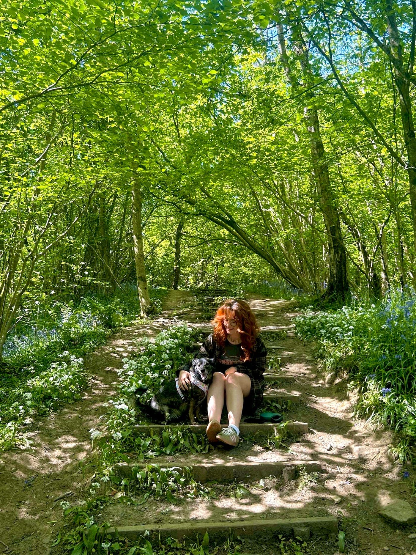 Chloe sitting with a dog on a bluebell woodland walk